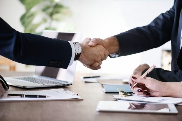 Two people shaking hands over a table of paperwork