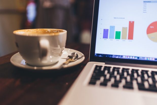 coffee cup next to open laptop displaying bar chart